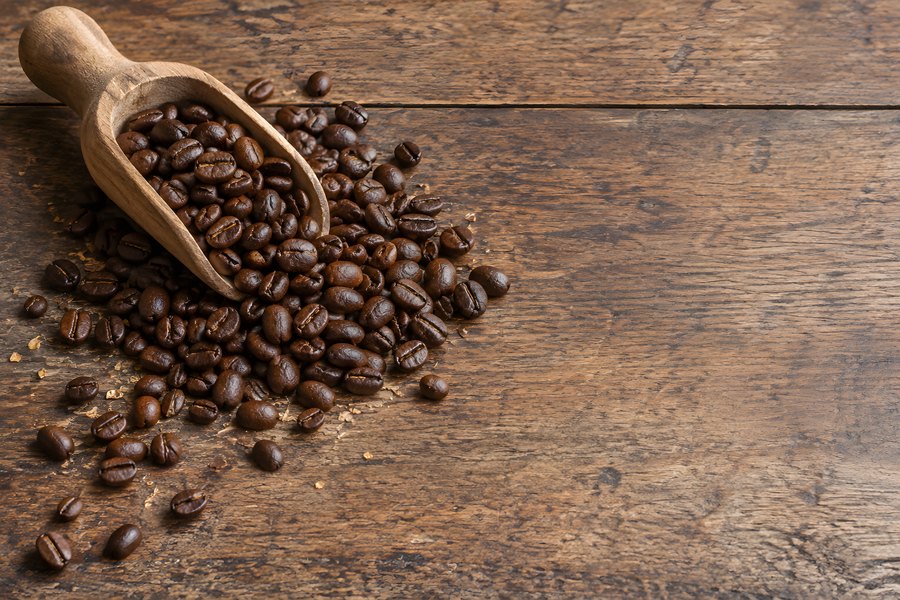 Roasted coffee beans spilling from a wooden scoop onto a rustic wood table with copy space