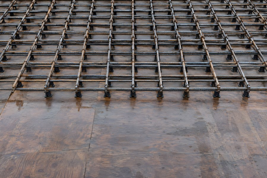 Steel rebar reinforcement mesh grid on wet plywood formwork before a concrete slab pour at a construction site