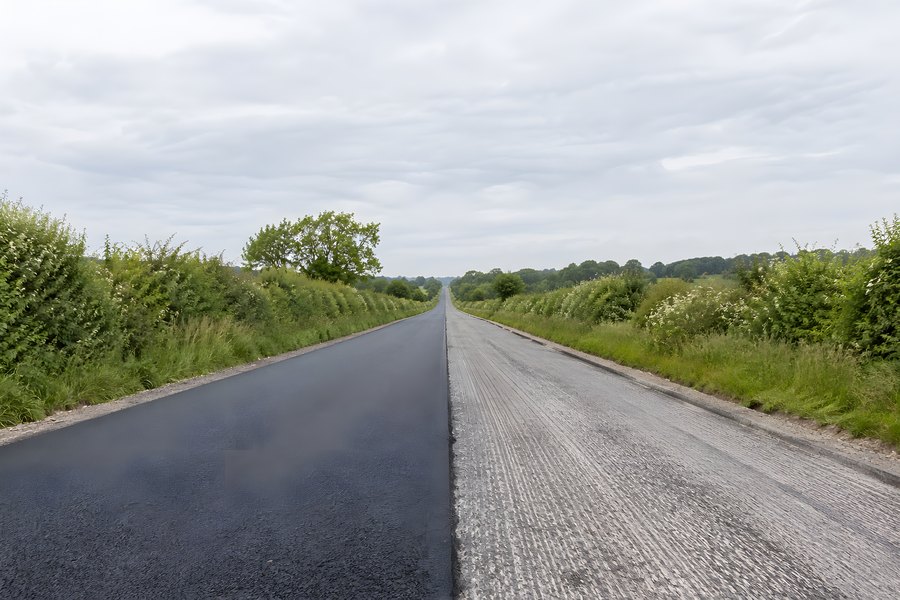 Rural road resurfacing project showing fresh black asphalt laid beside the old milled grey surface, no people