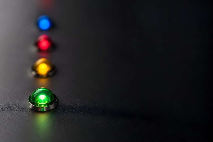 Glowing blue, red, amber and green indicator lights in a diagonal row against a dark background with copy space