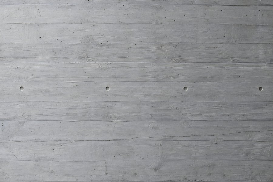 Board-formed raw concrete wall texture with wood grain pattern, tie holes and hairline crack