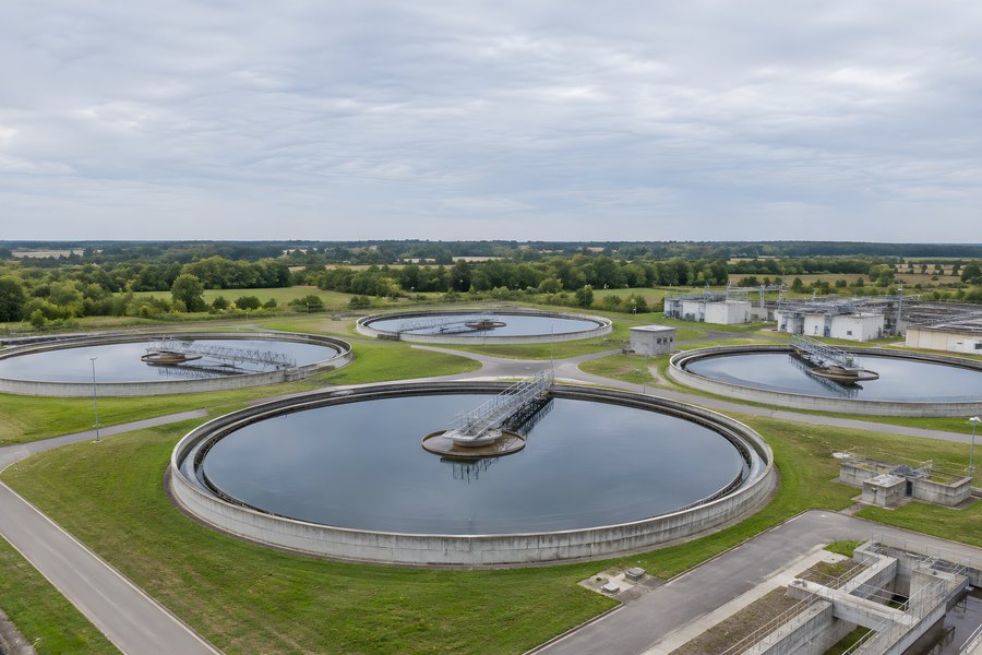 Aerial view of circular clarifier tanks at a wastewater treatment plant with rotating scraper bridges amid green fields