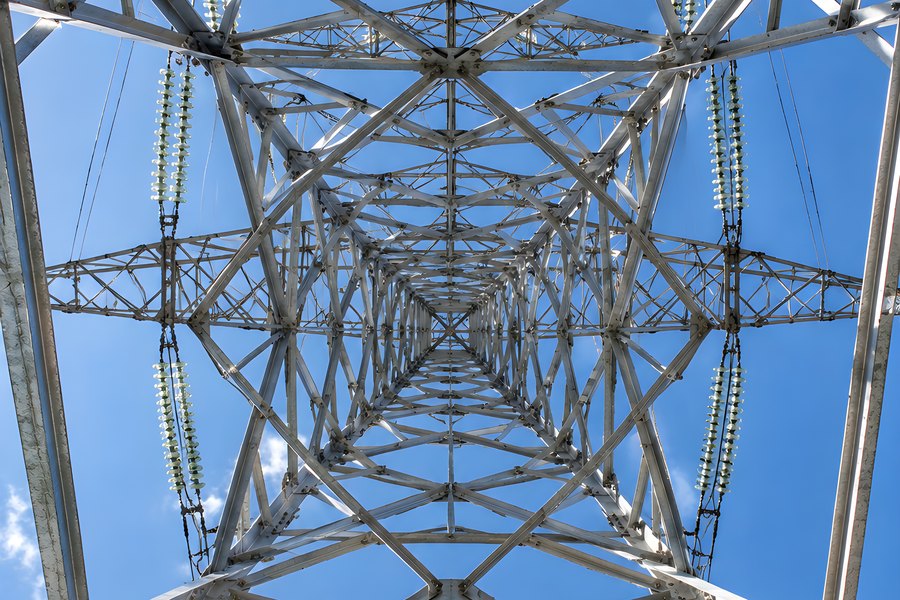 Low angle view up inside a steel lattice transmission tower with insulator strings and high voltage conductors against a blue sky