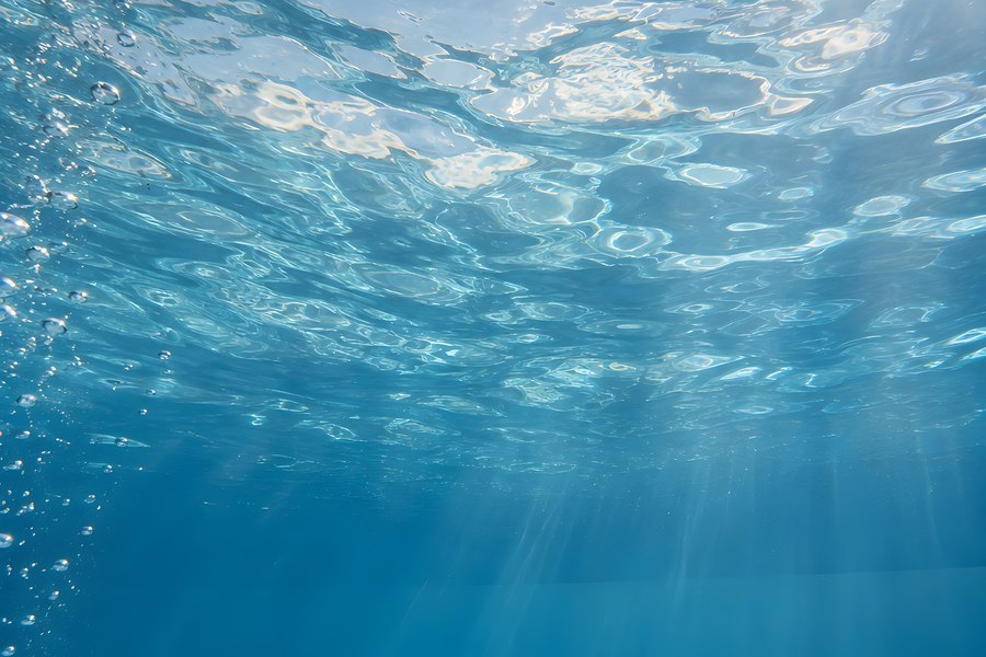 Underwater view of a sunlit swimming pool with rippling light caustics and rising bubbles